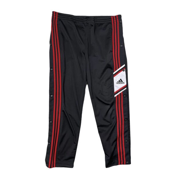 Pantalone tuta Adidas vintage da uomo nero con righe verticali rosse e bottoni neri ai lati e con logo Adidas nero su sfondo bianco sul lato sinistro, sopra le strisce