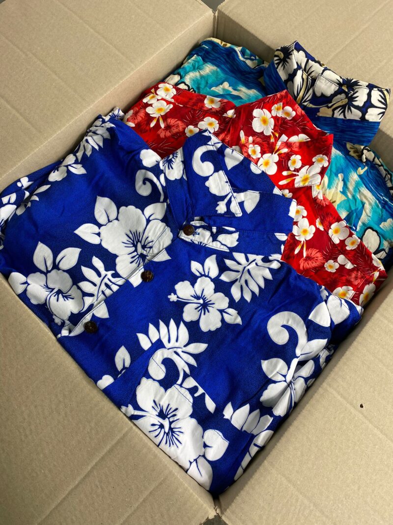 Tre camicie vintage hawaiiane da uomo nei colori blu elettrico rosso e verde acqua con fantasia a fiori all'interno di una scatola di cartone