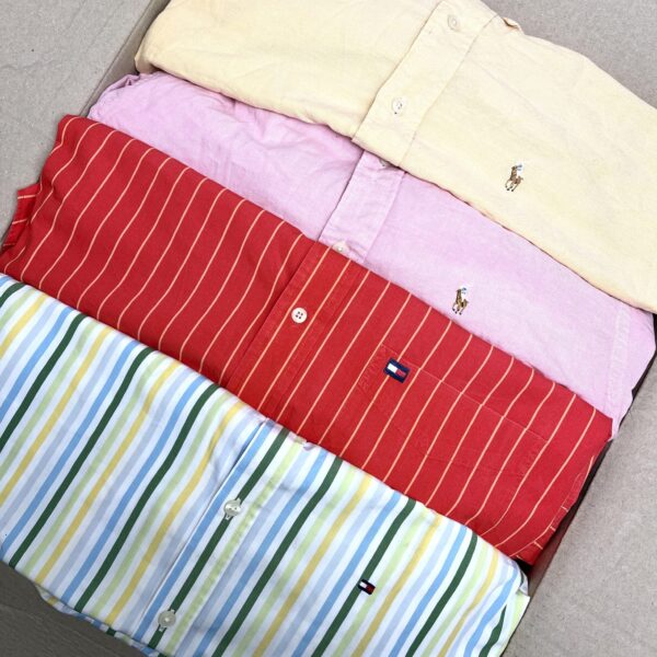Quattro camicie delle marche Ralph Lauren e Tommy Hilfigier piegate all'interno di una scatola di cartone, di cui una a righe bianche gialle azzurre e verdi, una rossa a righe bianche, una rosa e una gialla.