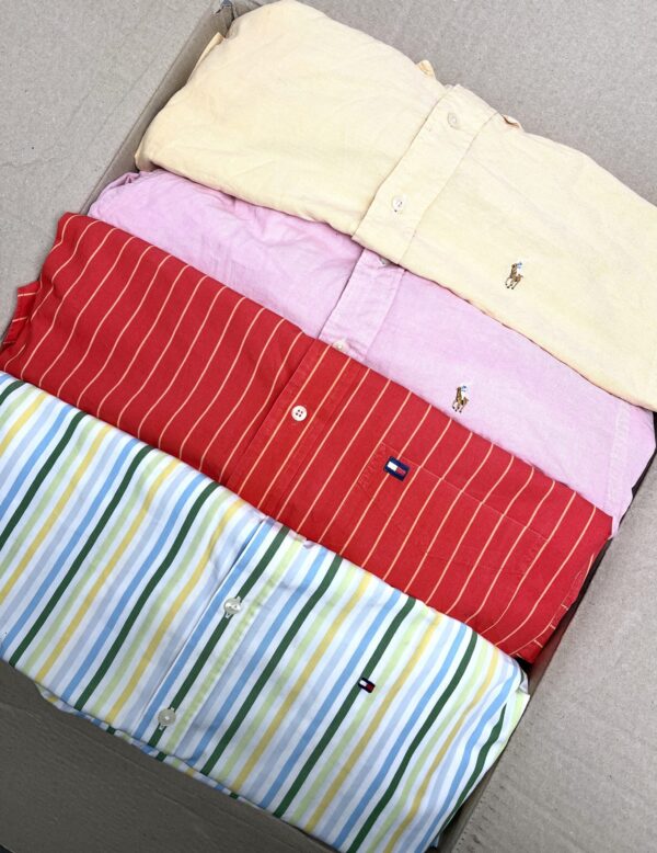Quattro camicie delle marche Ralph Lauren e Tommy Hilfigier piegate all'interno di una scatola di cartone, di cui una a righe bianche gialle azzurre e verdi, una rossa a righe bianche, una rosa e una gialla.